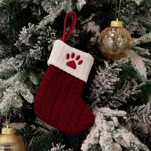 Detail of red knitted pet Christmas stocking with white cuff and paw print on snowy tree