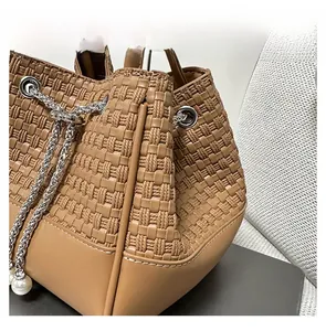 Detalle del bolso trenzado marrón con cordón plateado y colgante de perla decorativo