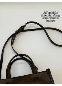 Détail du sac seau en cuir marron foncé avec bandoulière réglable et texture fine