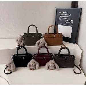 Fünf elegante Handtaschen in tiefen Tönen mit Metallschnallen und grauen Plüschhasen-Anhängern