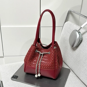 Détail du sac seau bordeaux avec texture tressée et cordon décoré d'une perle