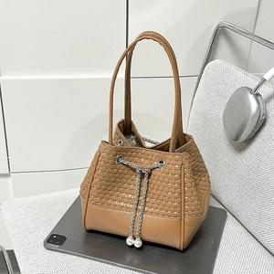 Détail du sac seau tressé beige avec cordon en chaîne argentée et accents de perles