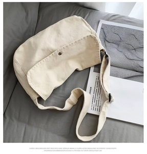 Detalle del bolso bandolera de lona crema con botón a presión de metal sobre un sofá gris