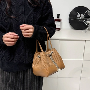 Détail de la texture en cuir marron tressé et lisse du sac seau avec chaîne de perles