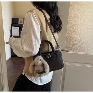 Detail einer dunkelbraunen Tasche mit Gürtelschnalle und süßem Plüschhasen-Anhänger