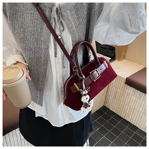 Detail van een bordeauxrode suède crossbodytas met decoratieve riem en hondenbedel