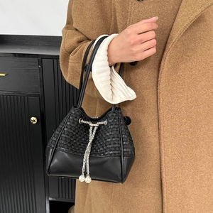 Détail du sac seau noir avec texture tressée et chaîne ornée d'une perle blanche