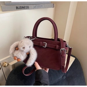 Detail der burgunderroten Handtasche mit mattem Lederfinish und grauem Kaninchen-Plüsch-Anhänger