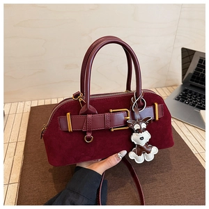 Detail van bordeauxrode suède handtas met gouden gesp en een honden hanger