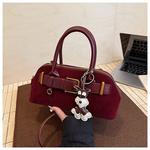 Detail van bordeauxrode suède tas met gouden hardware en schattige hondenhanger