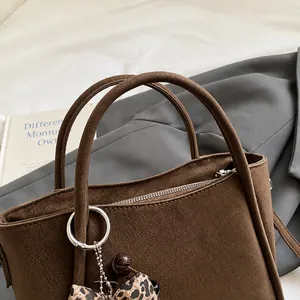 Detail of dark brown matte bucket bag with leopard scarf and metal ring on grey suit