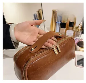 Detail of a brown crocodile pattern toiletry bag with golden zippers and a wide handle