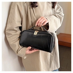 Detail of black crocodile texture handbag with gold double zippers in a lifestyle setting