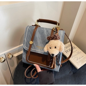 Detail van denim en lederen mini-rugzak met gouden hardware en een pluchen honden hanger