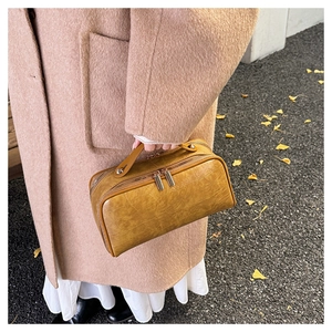 Detail of yellow crocodile pattern travel pouch held by a model in autumn street setting
