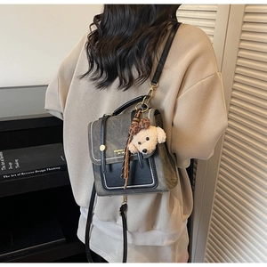 Detail van vintage grijs-zwarte crossbodytas met schattige hondenknuffel hanger aan zijkant