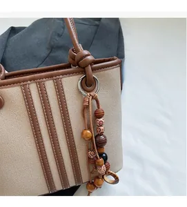 Detailed shot of beige canvas bucket bag with brown leather trim and wooden bead tassel decor