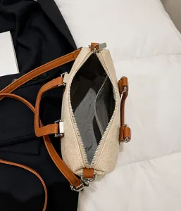 Detail view of beige woven barrel bag showing metal zipper closure and grey inner lining