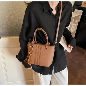 Close-up of brown leather bucket bag with vertical stitching and wooden bead tassel