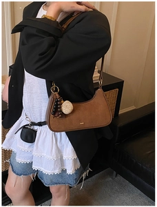 Brown suede underarm bag detail featuring gold logo and elegant bead shell pendant charm
