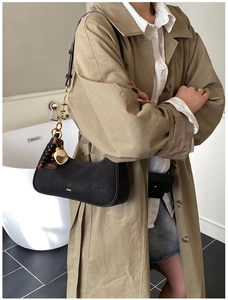 Minimalist black crescent shoulder bag featuring ethnic-style charms on khaki trench coat