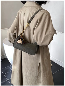 Detail of dark olive hobo bag with gold chain and vintage pendants on camel coat