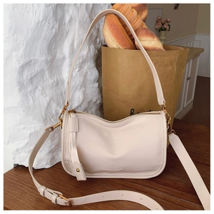 Detail view of cream white PU shoulder bag with gold hardware and adjustable strap on wood