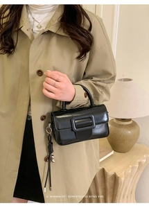 Close-up of minimalist black shiny leather square handbag with iconic leather wrapped buckle