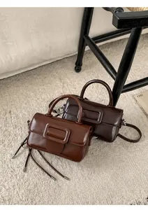 Detail view of two small square handbags in dark coffee and warm brown on a plush rug