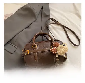 Dettaglio della borsa in pelle marrone con trama litchi e un ciondolo a orsetto