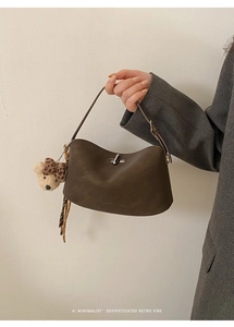 Close-up of minimalist dark coffee leather bag featuring a silver twist lock and bear charm