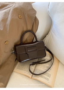 Deep brown retro minimalist square handbag displayed on an open book with a shoulder strap