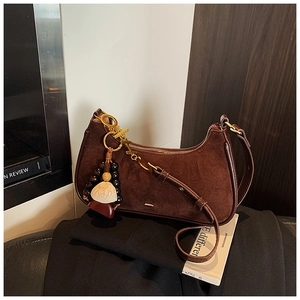 Close-up of dark brown suede crescent bag with shell pendant and gold hardware detail