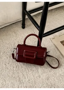 Deep red square leather handbag on a beige rug, featuring a shiny finish and decorative buckle