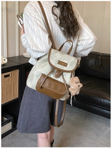 Rear view of a sage green vintage backpack with brown leather flap on a model's back