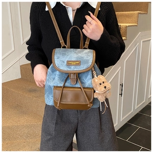 Detail of vintage denim backpack with brown leather flap and cute plush bear charm