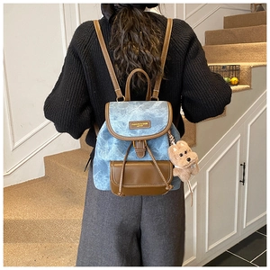 Detail of vintage denim backpack with brown leather accents and a plush bear charm