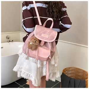 Pink faux leather backpack with plush bear charm worn by a model in a modern bathroom