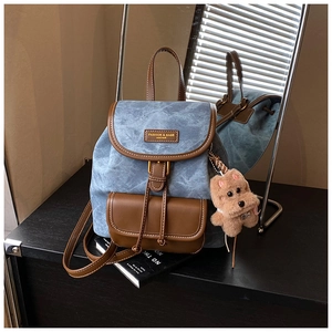 Detail of vintage denim backpack with brown leather trim and a cute plush puppy pendant