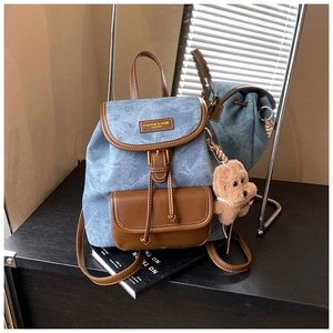 Detail of vintage denim blue mini backpack with brown trim and cute plush puppy charm