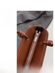 Detalle de cremallera metálica plateada y asa con nudo en un bolso de cuero marrón