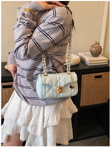 Detail of light blue quilted crossbody bag with gold chain strap and twist-lock clasp