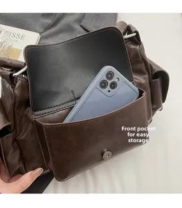 Detail view of brown faux leather shoulder bag featuring a functional front pocket for smartphone