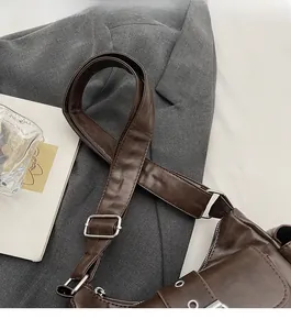 Close-up of brown matte leather shoulder bag with wide strap and silver metal eyelets