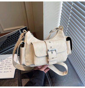 Detail view of cream multi-pocket crossbody bag with metallic silver buckles and wide strap