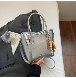 Detalle de bolso tote plateado texturizado con colgante de cuentas y correa de hombro