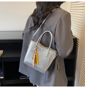 Detalle de bolso tote plateado metalizado con colgante de cuentas y correa ajustable