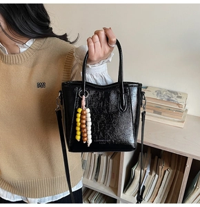 Detalle del bolso tote de cuero brillante negro con un adorno decorativo de cuentas de madera