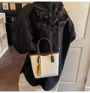 Bolso tote crema con ribete marrón y dije de cuentas coloridas llevado por una modelo