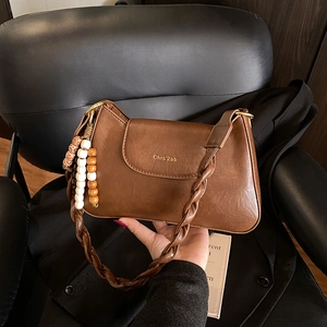 Bruine vintage baguette tas met gevlochten riem en kralenhanger in detailweergave